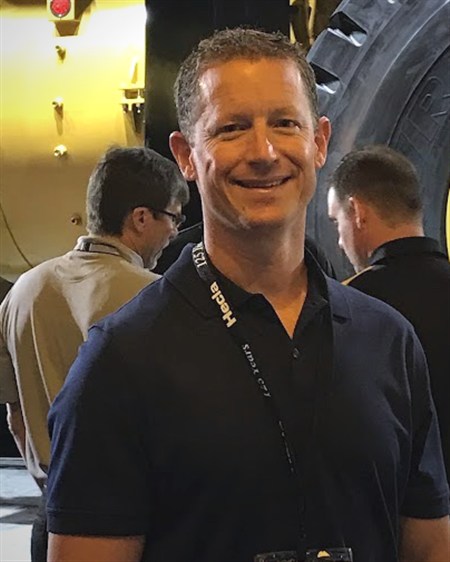 Darren Simoni, Principal of DSIM, in front of a haul truck at a mining industry show